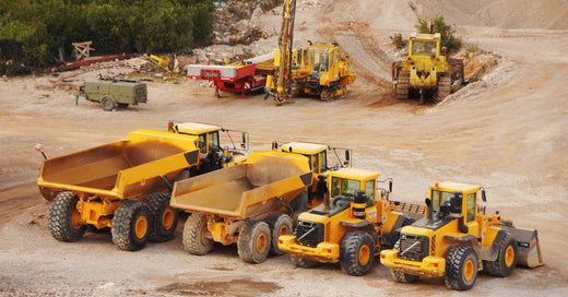 Various yellow heavy-duty machines, like dump trucks and bulldozers, at a dirt work area with a green generator nearby.