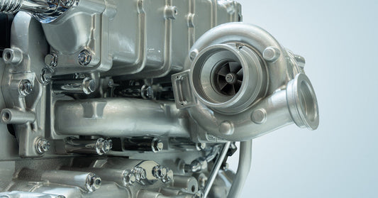 A close-up of a metallic turbocharger attached to a large diesel engine with the turbine and housing in view.
