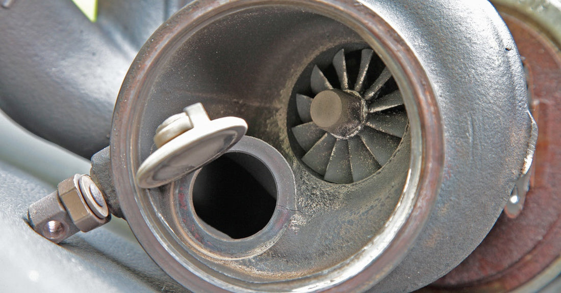 Close-up of a turbocharger with an open intake housing, showing turbine blades and metallic components with a worn texture.