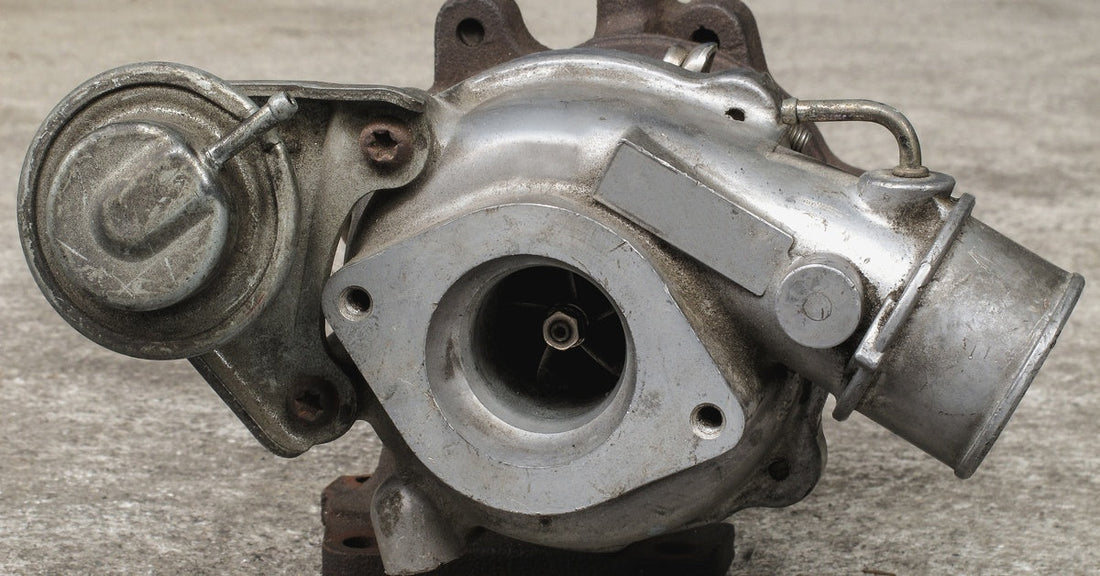 A close-up of a used turbocharger with some scratches and rusted areas sitting on top of a cement pad.