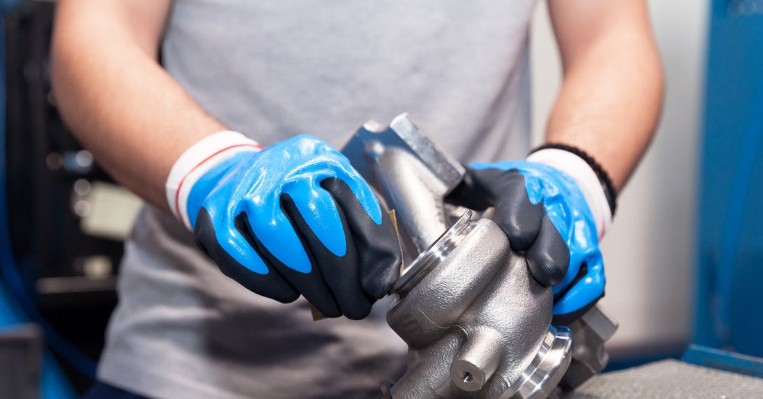 A person wearing blue rubber gloves and a gray T-shirt polishes a silver turbocharger with a small cloth.