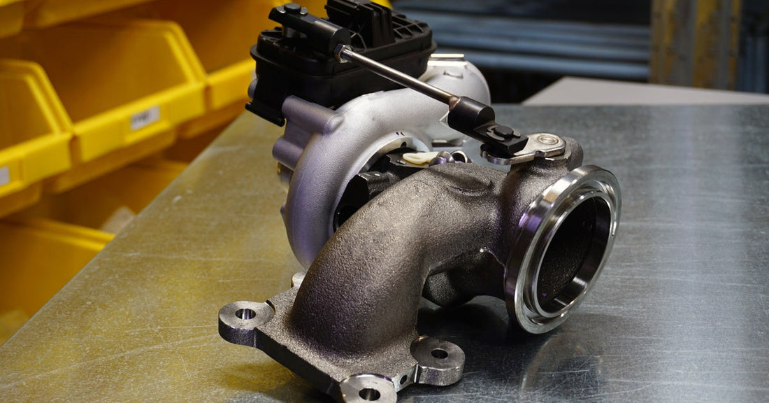A black and silver modern metal turbocharger sits on top of a steel table next to rows of yellow storage bins.