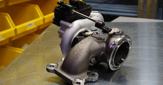 A black and silver modern metal turbocharger sits on top of a steel table next to rows of yellow storage bins.