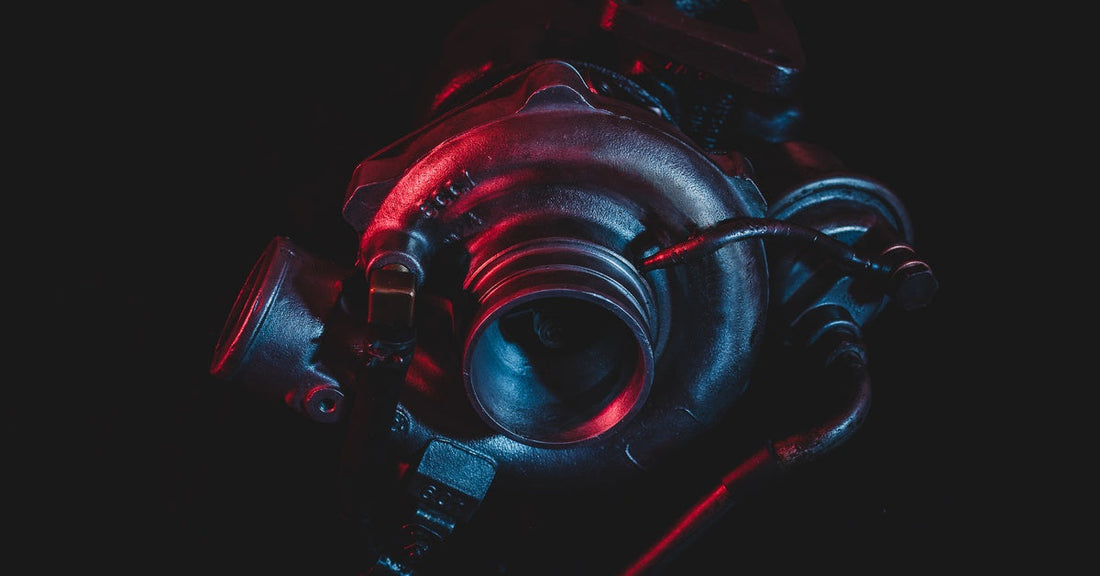 A sleek vehicle turbocharger shines with a blue and red light hitting the component against a black background.