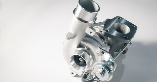 A sleek, silver turbocharger shines as the light source hits it, casting a shadow on a white background.