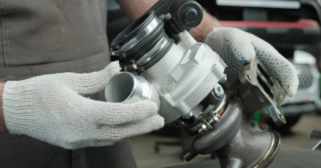 A person wearing white gloves holds and inspects a sleek, new turbocharger part placed on a black table.