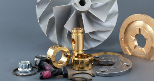 A set of turbocharger parts including a turbine compressor wheel, o-ring, bearings, and bushings against a gray background.