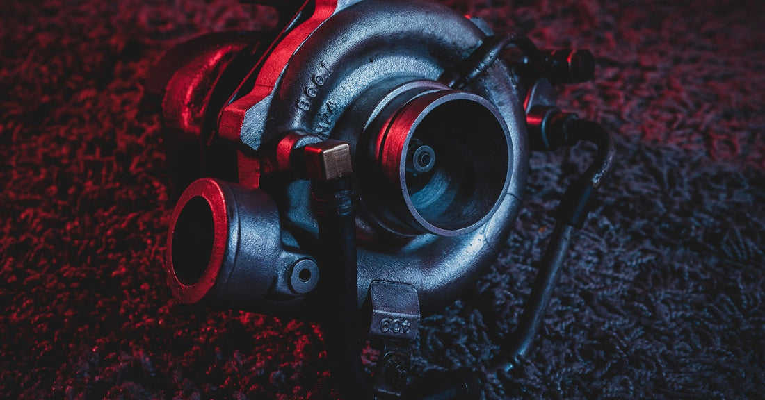 A red backlight reflects down on an old reconditioned turbocharger that is sitting on a black carpet.