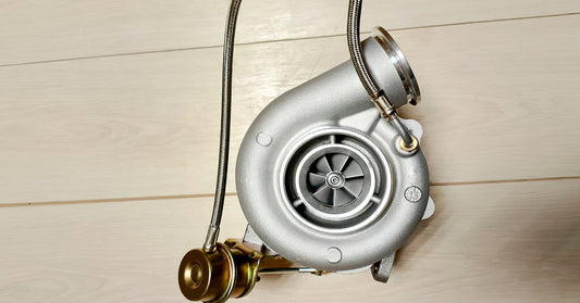 The light shines down on a turbocharger with a gold wastegate actuator siting on top of a white wooden floor.