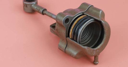 A worn-out turbocharger actuator is partially split, showing the components inside, sitting against a pink background.