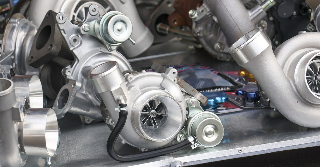 Multiple new, modern vehicle turbochargers sit on top of a metal floor, glistening in an automotive workshop.
