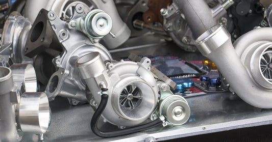 Multiple new, modern vehicle turbochargers sit on top of a metal floor, glistening in an automotive workshop.