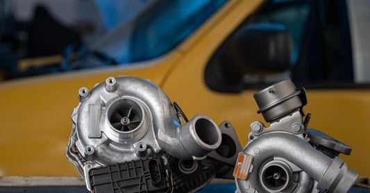 Components of turbocharger for a diesel engine sit on top of a black table. Behind the parts is a yellow vehicle.