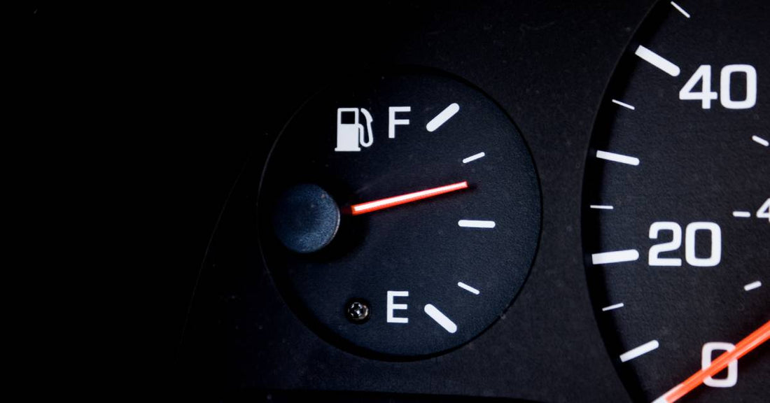 A fuel gauge on the left side of a speedometer on a car's dashboard. The needle points above the mark for a half-full tank.