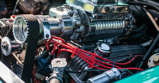The open hood of a light blue car has the engine exposed. A supercharger is installed to the engine's top.