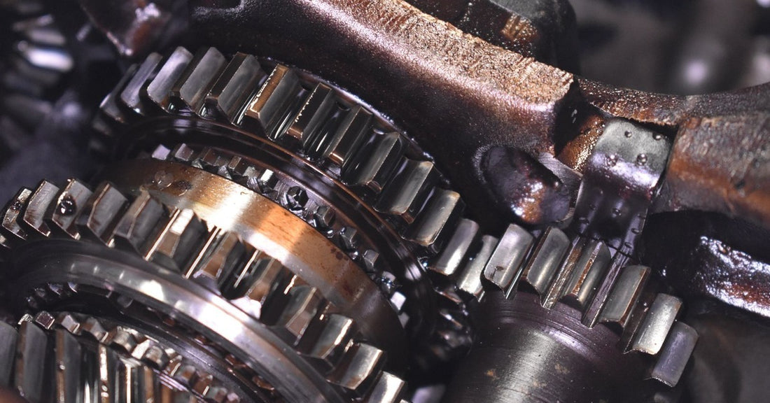 The interior of a damaged car engine. The gears and sprockets show signs of wear and corrosion, revealing small broken parts.