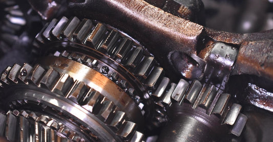 The interior of a damaged car engine. The gears and sprockets show signs of wear and corrosion, revealing small broken parts.
