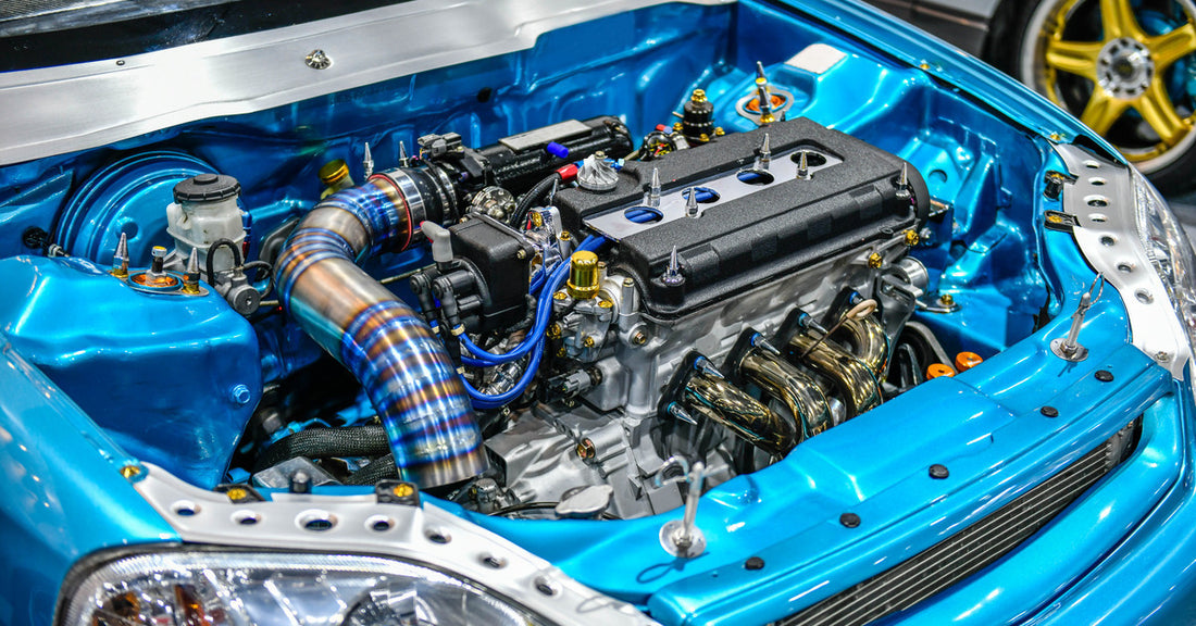 A bright blue-colored custom car with the engine bay open showing a turbocharger and detailed piping work.
