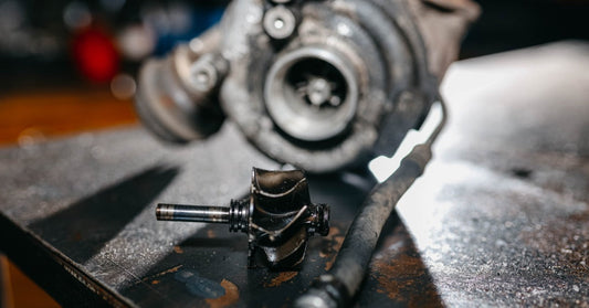The turbine of a turbocharger sits on top of a workshop table for repairs. Behind it is a blurred-out turbocharger.