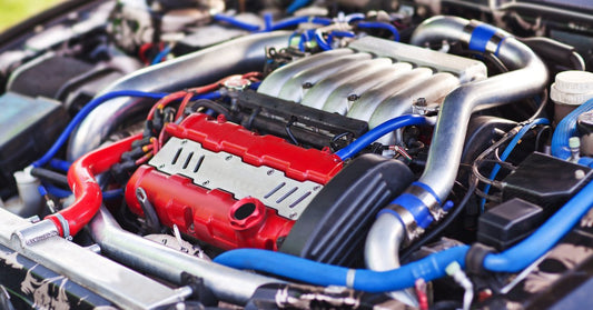 A turbocharged car engine with red and silver pipes, black hoses, and metal components arranged under an open hood.